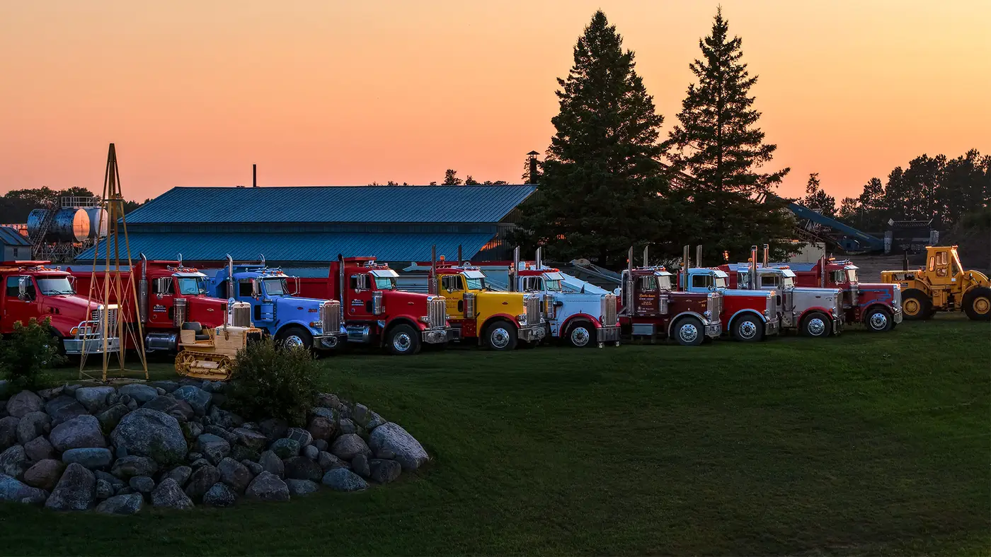 Storlie Construction's dump trucks and a loader lined up at sunset in Cass Lake, Minnesota